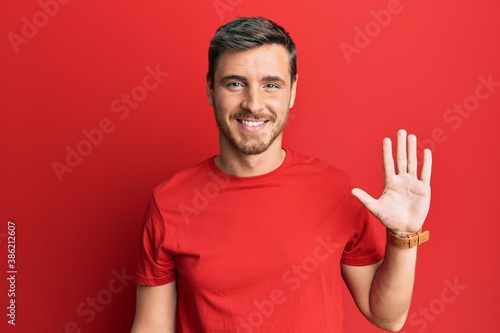 Handsome caucasian man wearing casual red tshirt showing and pointing up with fingers number five while smiling confident and happy.