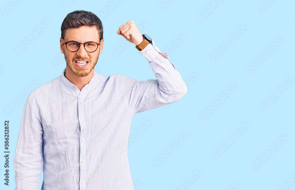 Handsome young man with bear wearing elegant business shirt and glasses angry and mad raising fist frustrated and furious while shouting with anger. rage and aggressive concept. Handsome young man with bear wearing elegant business shirt and glasses angry and mad raising fist frustrated and furious while shouting with anger. rage and aggressive concept.