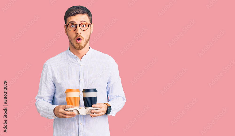 Handsome young man with bear holding takeaway cup of coffee scared and amazed with open mouth for surprise, disbelief face Handsome young man with bear holding takeaway cup of coffee scared and amazed with open mouth for surprise, disbelief face