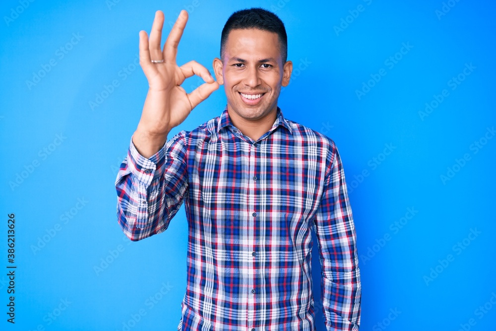 Young handsome latin man wearing casual clothes smiling positive doing ok sign with hand and fingers. successful expression. Young handsome latin man wearing casual clothes smiling positive doing ok sign with hand and fingers. successful expression.