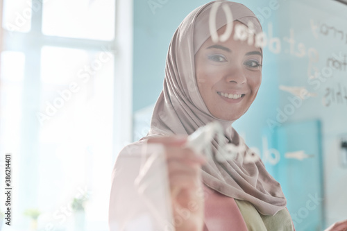 Young smiling Muslim female broker in hijab making notes with highlighter photo