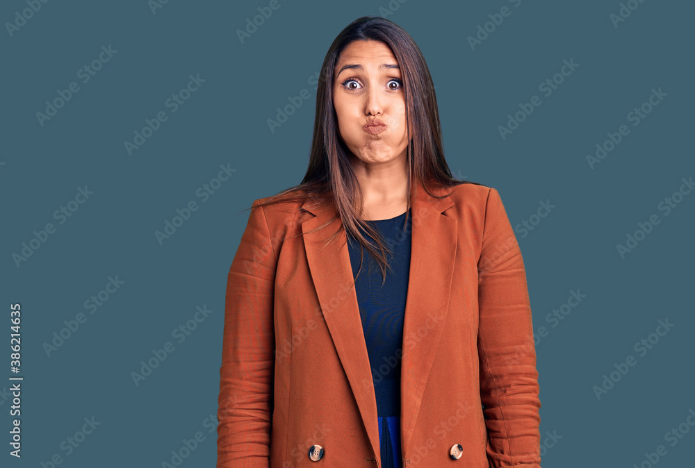 Young beautiful brunette woman wearing elegant clothes puffing cheeks with funny face. mouth inflated with air, crazy expression. Young beautiful brunette woman wearing elegant clothes puffing cheeks with funny face. mouth inflated with air, crazy expression.