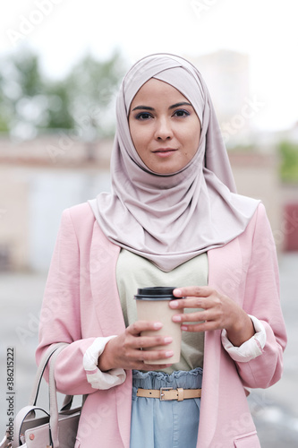 Young gorgeous female in hijab, pullover, pants and pink cardigan having coffee photo
