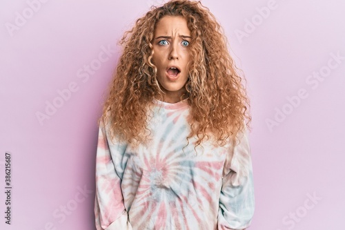 Beautiful caucasian teenager girl wearing casual tie dye sweatshirt scared and amazed with open mouth for surprise, disbelief face