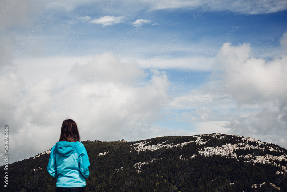 a young girl in a blue jacket stands high in the mountains and enjoys the view, enjoy the beauty of nature, people in the mountains, peace and tranquility