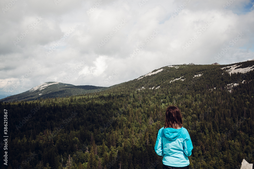 a young girl in a blue jacket stands high in the mountains and enjoys the view, enjoy the beauty of nature, people in the mountains, peace and tranquility