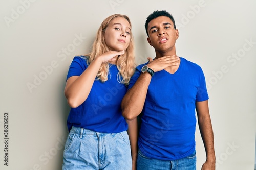 Young interracial couple wearing casual clothes cutting throat with hand as knife, threaten aggression with furious violence