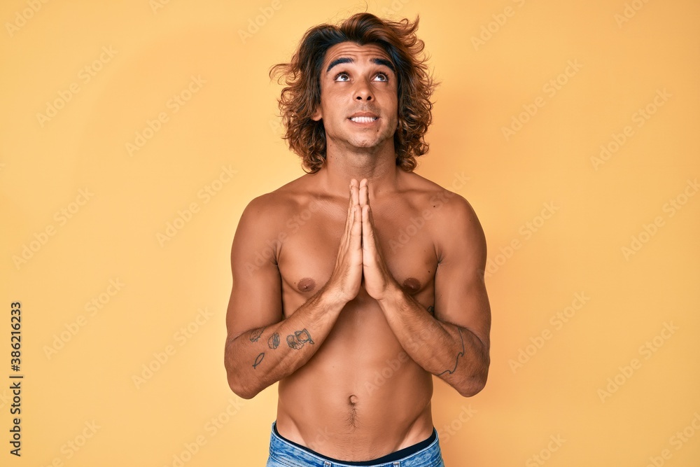 Young hispanic man standing shirtless begging and praying with hands together with hope expression on face very emotional and worried. begging.