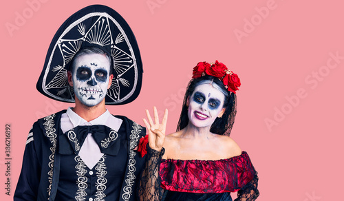Young couple wearing mexican day of the dead costume over background showing and pointing up with fingers number four while smiling confident and happy.