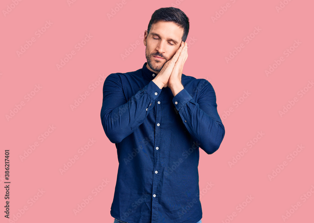 Young handsome man wearing casual shirt sleeping tired dreaming and posing with hands together while smiling with closed eyes. Young handsome man wearing casual shirt sleeping tired dreaming and posing with hands together while smiling with closed eyes.