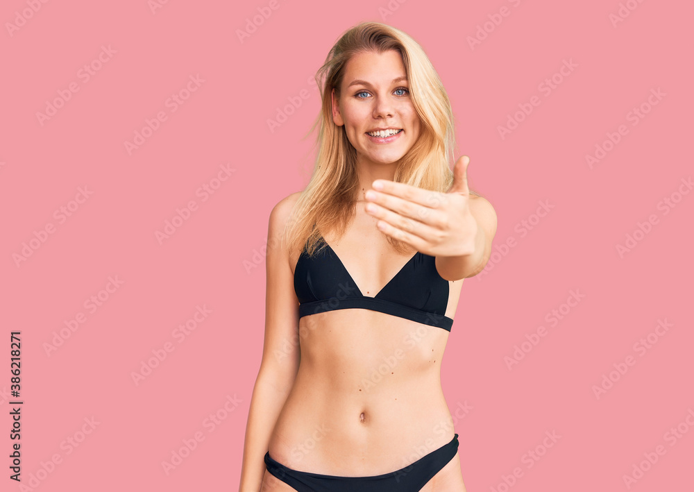 Naklejka premium Young beautiful blonde woman wearing bikini smiling friendly offering handshake as greeting and welcoming. successful business.