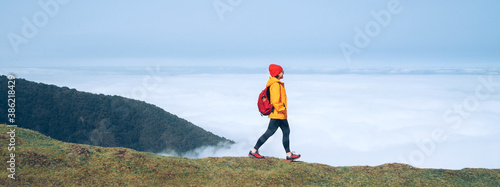 Young female backpacker dressed orange waterproof jacket hiking by the mountain above the cloud route at the end of February on Madeira island, Portugal. Active people around  World traveling concept. photo