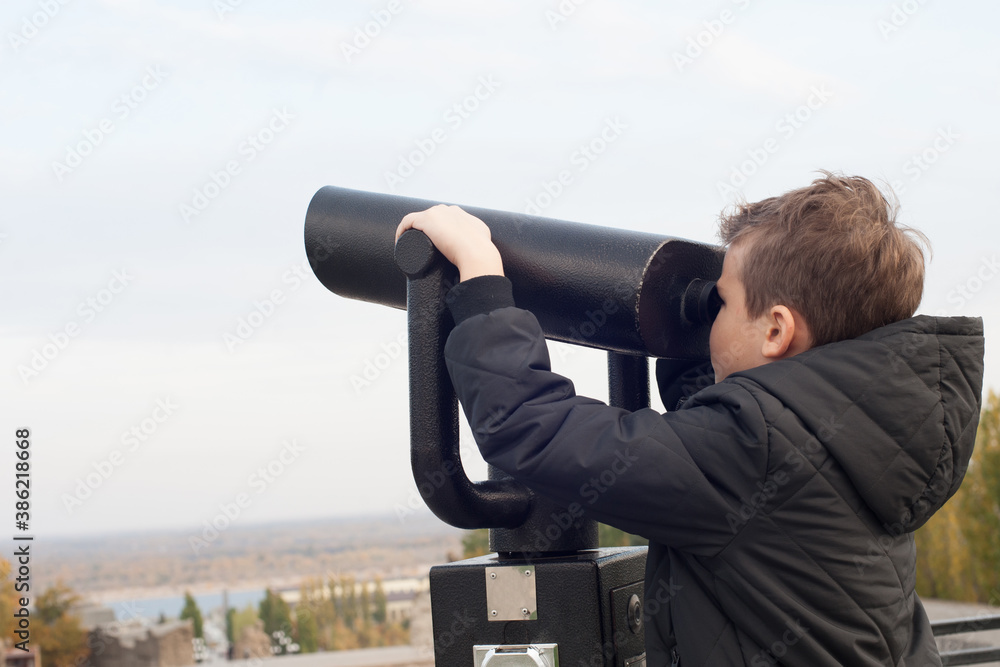 a boy with a black jacket on the observation deck looks through binoculars