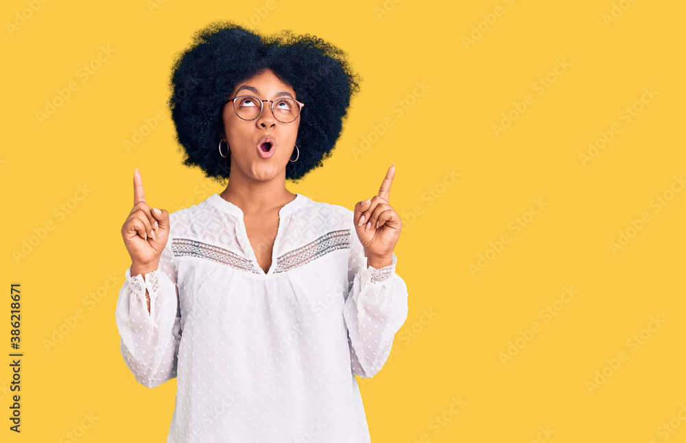 Young african american girl wearing casual clothes amazed and surprised looking up and pointing with fingers and raised arms. Young african american girl wearing casual clothes amazed and surprised looking up and pointing with fingers and raised arms.