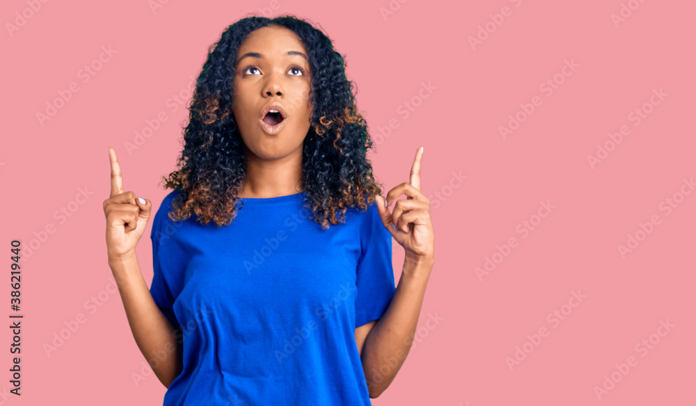 Young african american woman wearing casual clothes amazed and surprised looking up and pointing with fingers and raised arms. Young african american woman wearing casual clothes amazed and surprised looking up and pointing with fingers and raised arms.
