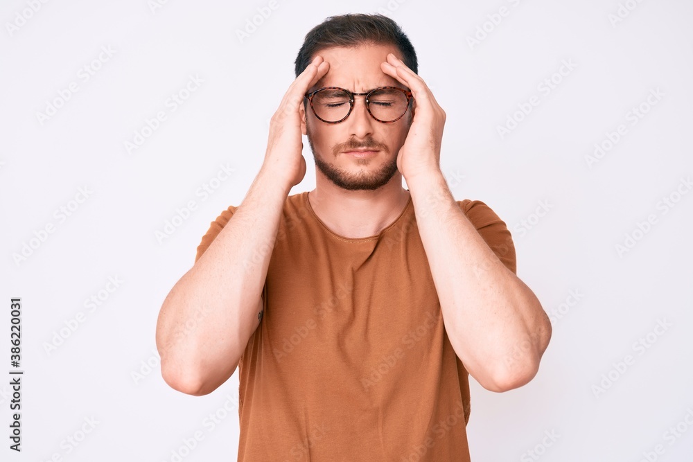 Young handsome man wearing casual clothes and glasses suffering from headache desperate and stressed because pain and migraine. hands on head. Young handsome man wearing casual clothes and glasses suffering from headache desperate and stressed because pain and migraine. hands on head.