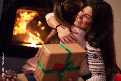 Girl friends exchanging Christmas presents over fireplace