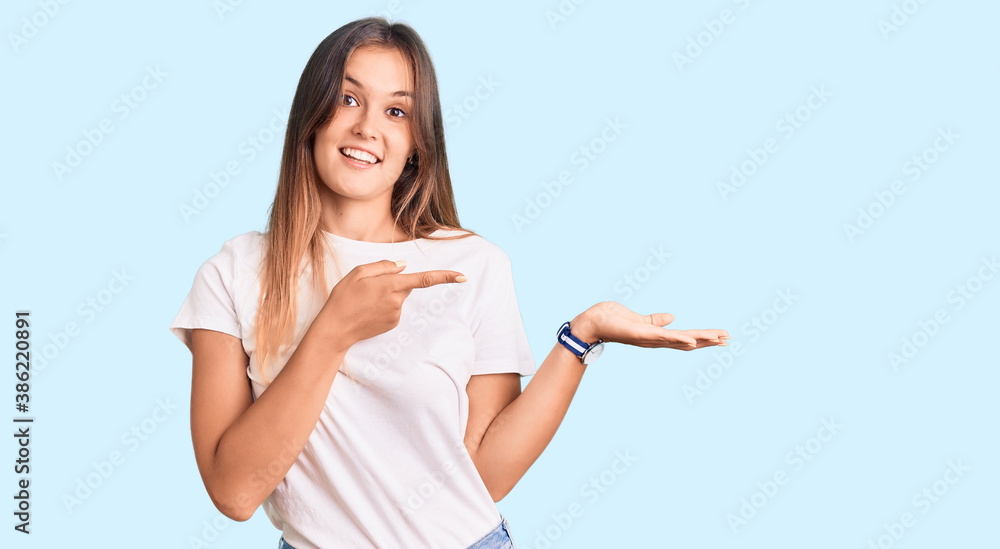Plakat Piękna kaukaska kobieta ubrana w dorywczo białą koszulkę zdumiona i uśmiechnięta do kamery, prezentując ręką i wskazując palcem.