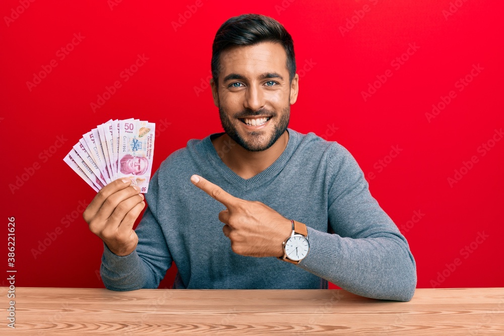 Handsome hispanic man holding mexican pesos smiling happy pointing with hand and finger Handsome hispanic man holding mexican pesos smiling happy pointing with hand and finger