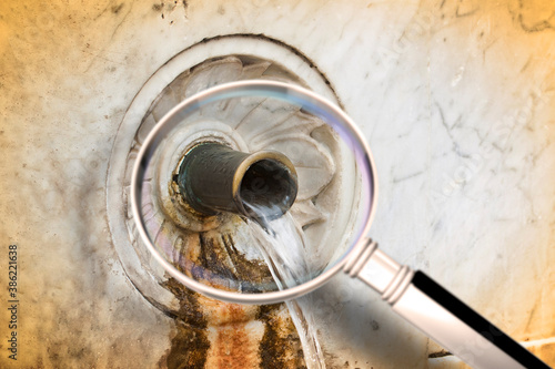 Checking the water purity of public drinking fountains - Are drinking fountains safe and free from germs, bacteria and virus? - concept image with water gushing as seen from a magnifying glass
