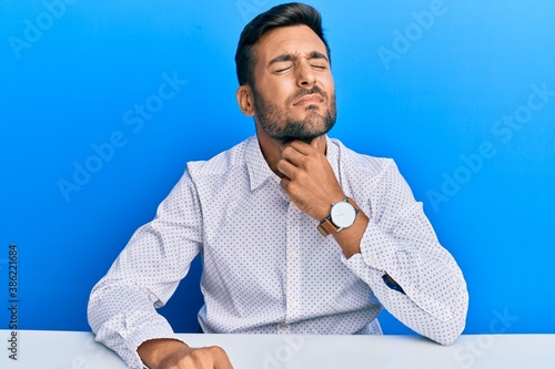 Handsome hispanic man wearing business clothes sitting on the table touching painful neck, sore throat for flu, clod and infection photo