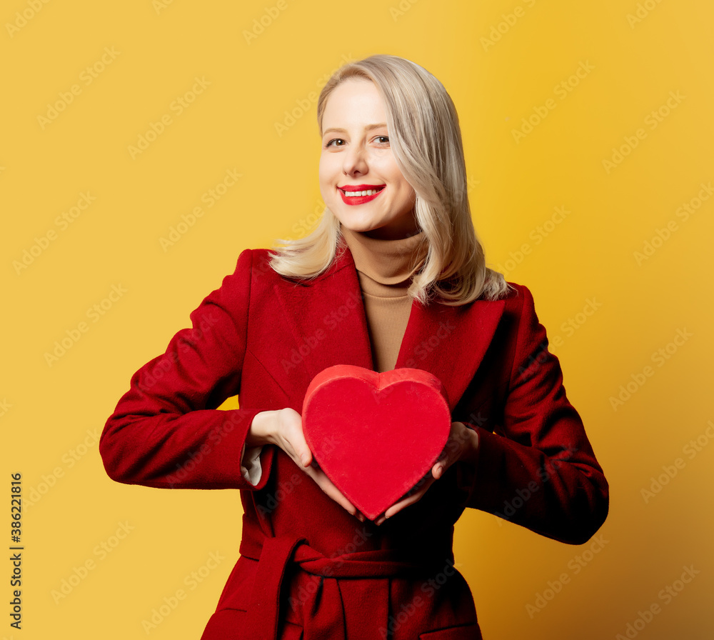 woman in red coat with gift box on yellow background woman in red coat with gift box on yellow background