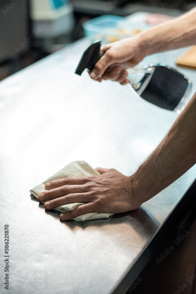 Hands of contemporary chef of restaurant spraying sanitizer on kitchen table Hands of contemporary chef of restaurant spraying sanitizer on kitchen table
