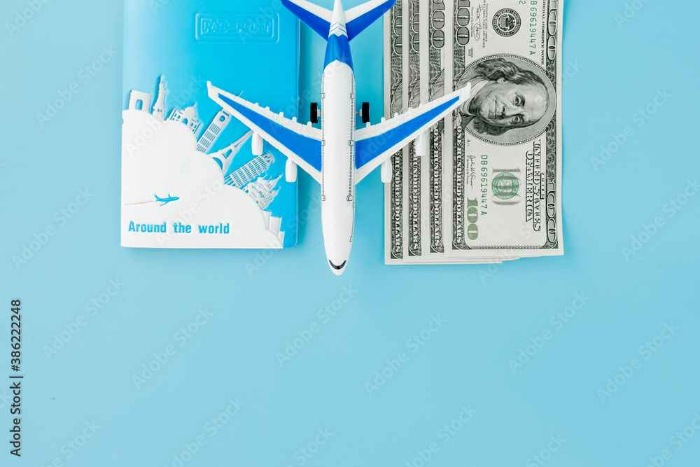 Passport with model of passenger plane and dollars on blue background. Travel concept, copy space.