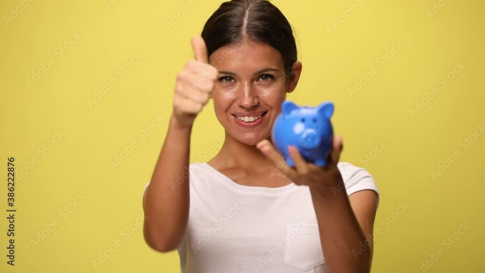 casual woman presenting her piggy bank, giving a thumbs up on yellow background casual woman presenting her piggy bank, giving a thumbs up on yellow background
