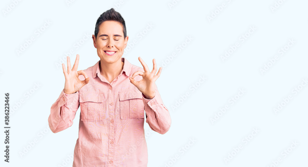 Young woman with short hair wearing casual clothes relaxed and smiling with eyes closed doing meditation gesture with fingers. yoga concept. Young woman with short hair wearing casual clothes relaxed and smiling with eyes closed doing meditation gesture with fingers. yoga concept.