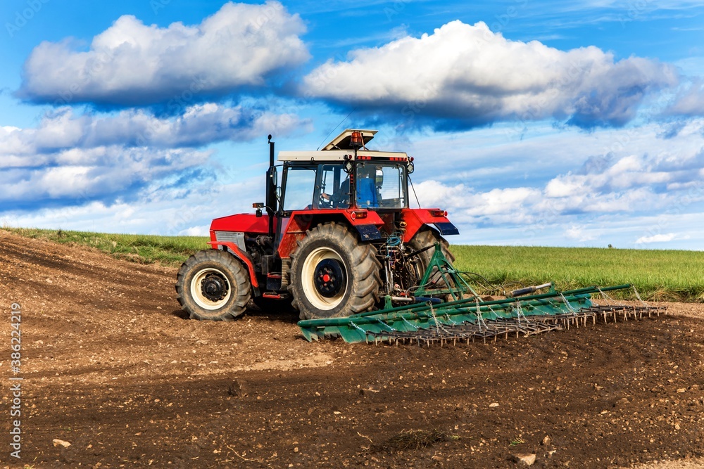 Agriculture red tractor cultivating field over blue sky. Old red tractor in the agricultural field; mechanism. Tractor plowing land. Harvester sowing wheat. Agriculture red tractor cultivating field over blue sky. Old red tractor in the agricultural field; mechanism. Tractor plowing land. Harvester sowing wheat.