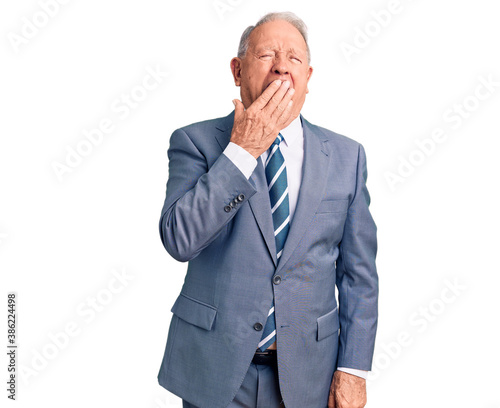 Senior handsome grey-haired man wearing elegant suit bored yawning tired covering mouth with hand. restless and sleepiness.