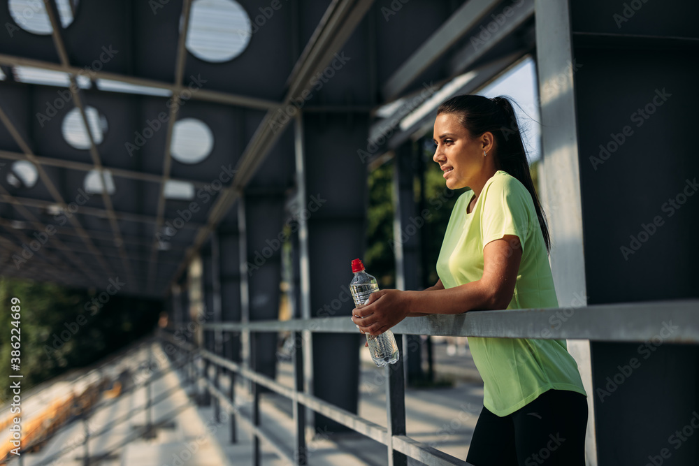 Sporty woman with bottle of water resting after training