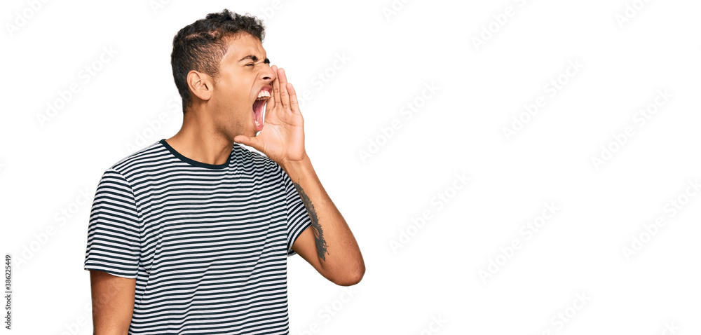 Young handsome african american man wearing casual clothes shouting and screaming loud to side with hand on mouth. communication concept. Young handsome african american man wearing casual clothes shouting and screaming loud to side with hand on mouth. communication concept.