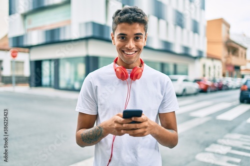 Papier peint Young latin man smiling happy using smartphone and headphones at the city