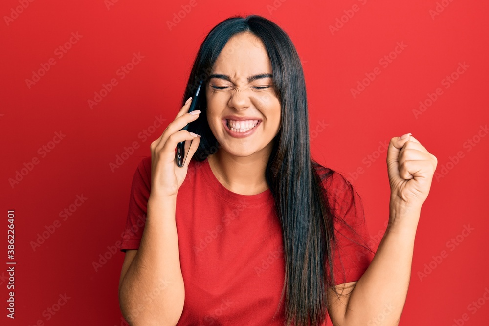 Young beautiful hispanic girl having conversation talking on the smartphone screaming proud, celebrating victory and success very excited with raised arm Young beautiful hispanic girl having conversation talking on the smartphone screaming proud, celebrating victory and success very excited with raised arm
