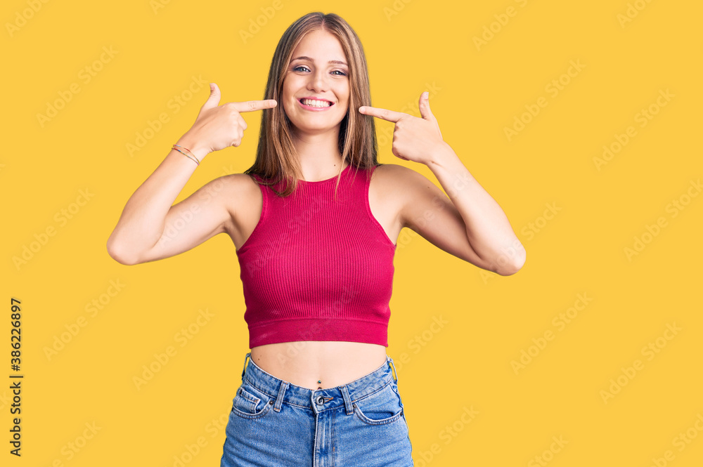 Young beautiful blonde woman wearing elegant summer shirt smiling cheerful showing and pointing with fingers teeth and mouth. dental health concept. Young beautiful blonde woman wearing elegant summer shirt smiling cheerful showing and pointing with fingers teeth and mouth. dental health concept.
