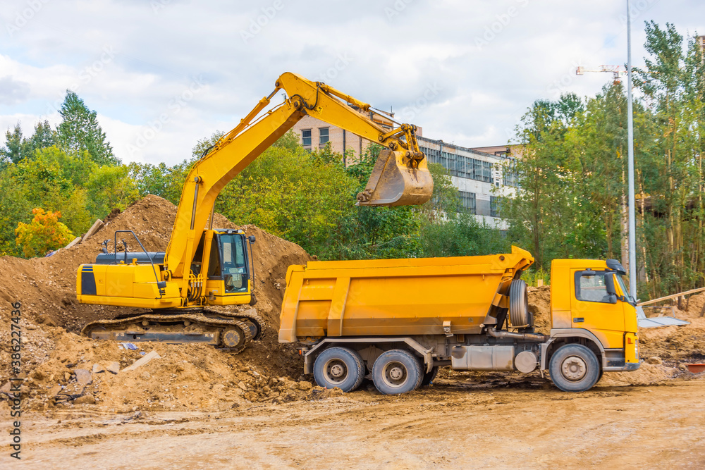 Yellow truck and excavator load soil with sand during road construction in urban area. Yellow truck and excavator load soil with sand during road construction in urban area.