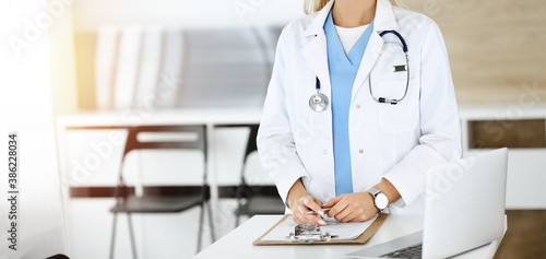 Unknown woman-doctor at work in sunny clinic. Female physician controls medication history record, close-up. Medicine concept