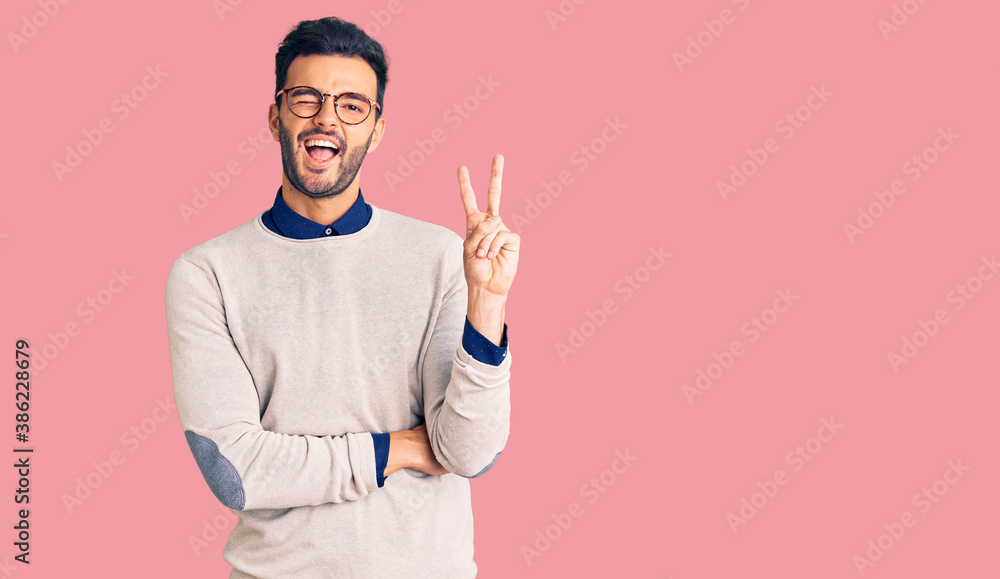Young handsome hispanic man wearing elegant clothes and glasses smiling with happy face winking at the camera doing victory sign. number two. Young handsome hispanic man wearing elegant clothes and glasses smiling with happy face winking at the camera doing victory sign. number two.