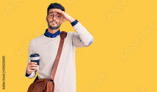 Young handsome hispanic man wearing leather bag and drinking take away coffee stressed and frustrated with hand on head, surprised and angry face