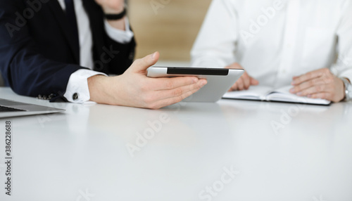 Unknown business people using tablet computer in modern office. Businessman or male entrepreneur is working with his colleague at the desk