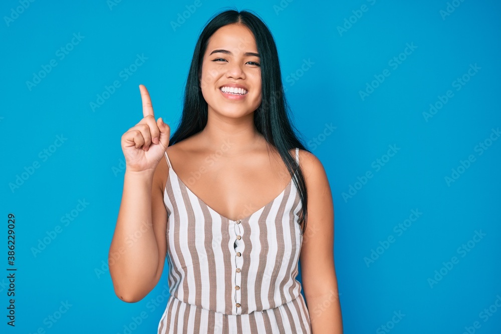 Young beautiful asian girl wearing casual clothes showing and pointing up with finger number one while smiling confident and happy. Young beautiful asian girl wearing casual clothes showing and pointing up with finger number one while smiling confident and happy.