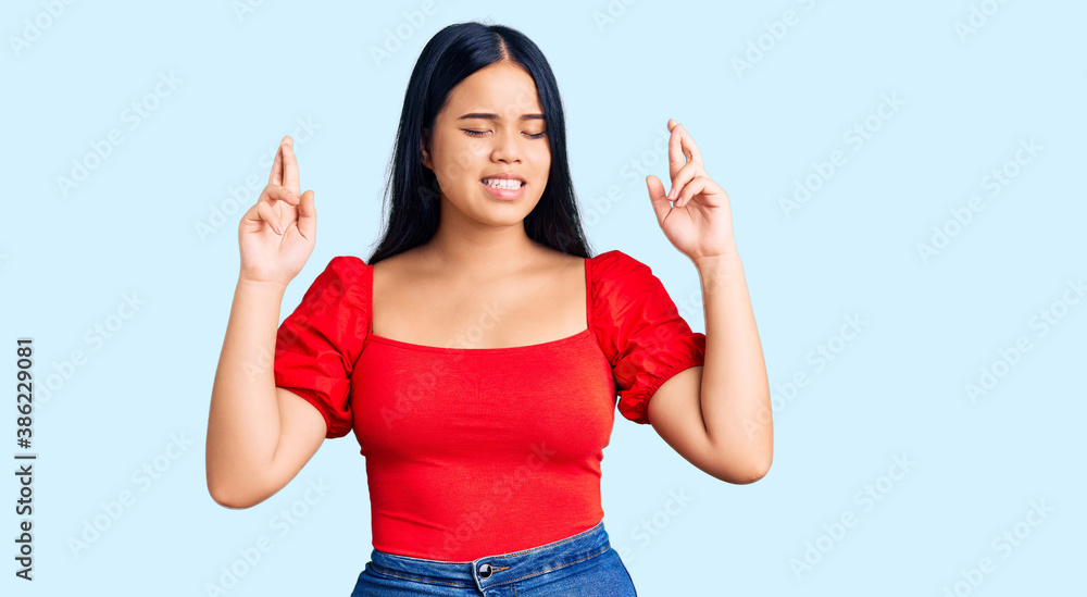 Young beautiful asian girl wearing casual clothes gesturing finger crossed smiling with hope and eyes closed. luck and superstitious concept. Young beautiful asian girl wearing casual clothes gesturing finger crossed smiling with hope and eyes closed. luck and superstitious concept.