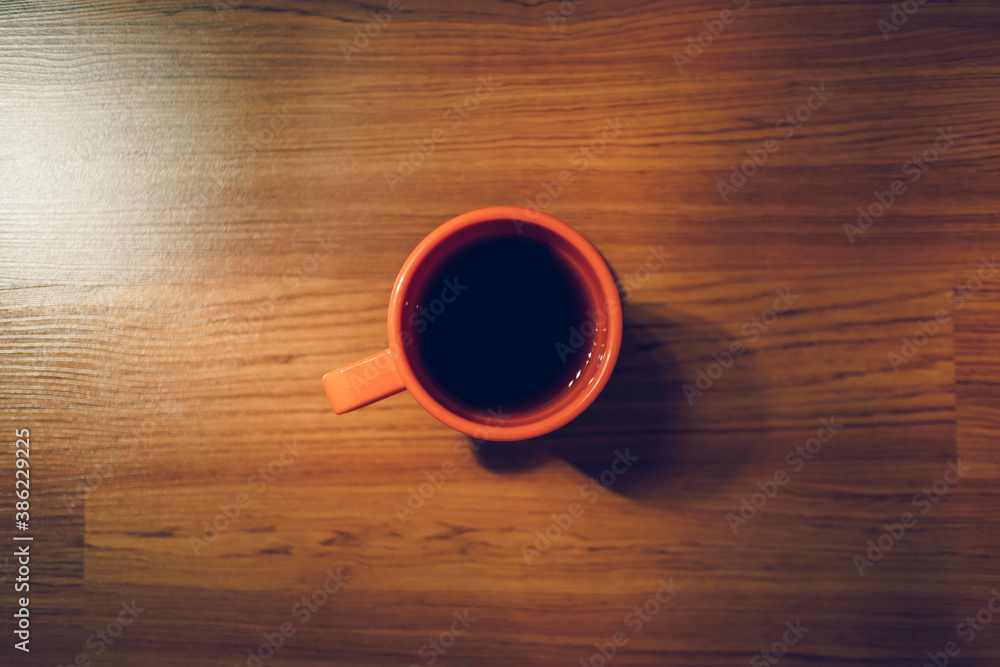 Orange hot coffee mug on the wooden floor in low light room.