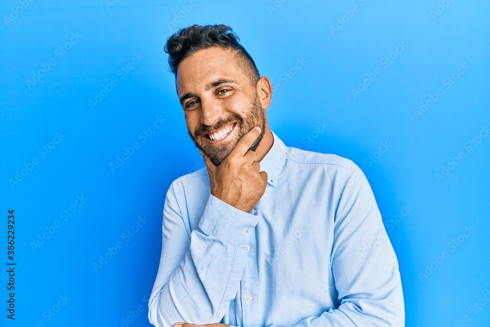 Handsome man with beard wearing casual clothes looking confident at the camera smiling with crossed arms and hand raised on chin. thinking positive. Handsome man with beard wearing casual clothes looking confident at the camera smiling with crossed arms and hand raised on chin. thinking positive.