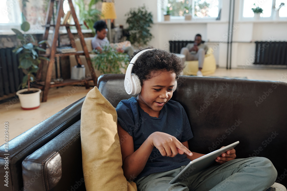 Adorable little boy with headphones pointing at screen of digital tablet at home