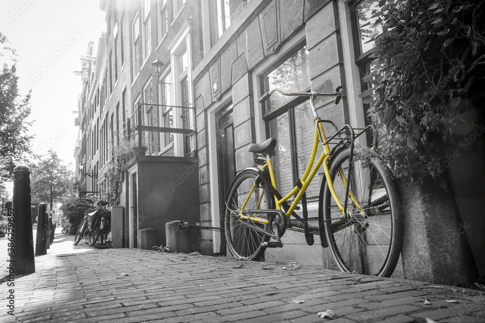 A picture of a lonely yellow bike on the bridge over the channel in Amsterdam. The background is black and white.