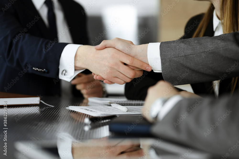 Unknown businessman shaking hands with his colleague or partner above the glass desk in modern office, close-up. Business people group at meeting Unknown businessman shaking hands with his colleague or partner above the glass desk in modern office, close-up. Business people group at meeting