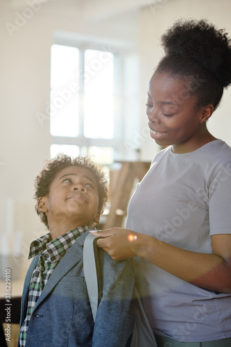 Happy young careful mother in casualwear helping her little son with backpack